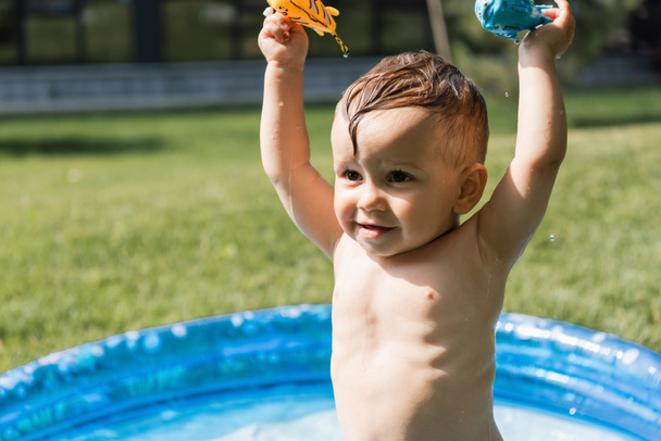 χαρούμενο μικρό παιδί κρατώντας παιχνίδια από καουτσούκ πάνω από το κεφάλι έξω - Φωτογραφία, εικόνα