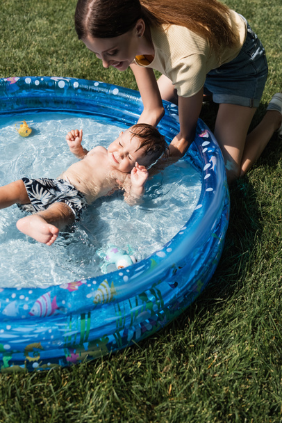 high angle view of happy mother bathing toddler son in inflatable pool - 写真・画像