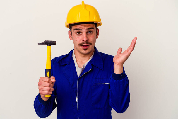 Young caucasian worker man holding a hammer isolated on white background surprised and shocked. - Fotoğraf, Görsel