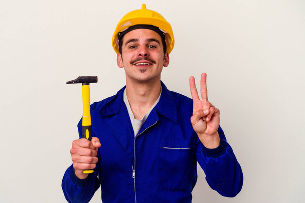 Junger kaukasischer Arbeiter mit einem Hammer auf weißem Hintergrund, der die Nummer zwei mit den Fingern zeigt. - Foto, Bild
