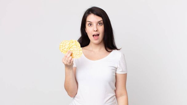 pretty woman looking very shocked or surprised and holding a diet rice cakes - Foto, immagini