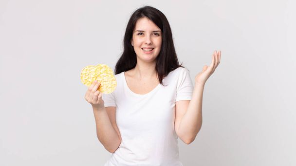 όμορφη γυναίκα αισθάνεται ευτυχισμένη, έκπληκτος συνειδητοποιώντας μια λύση ή ιδέα και κρατώντας ένα κέικ ρυζιού δίαιτα - Φωτογραφία, εικόνα