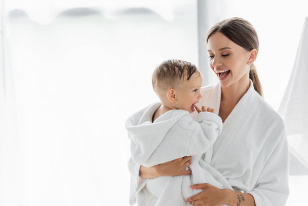 amazed mother looking at toddler son in bathrobe - Foto, Imagen