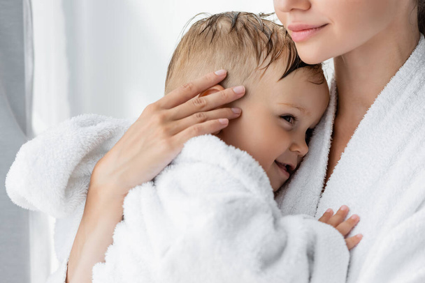 young mother holding in arms happy toddler son in bathrobe - Foto, Imagem