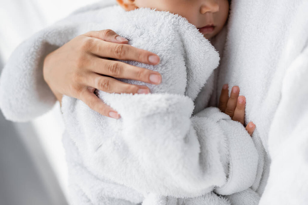 levágott kilátás fiatal anya gazdaság karban kisgyermek fia fürdőköpenyben - Fotó, kép