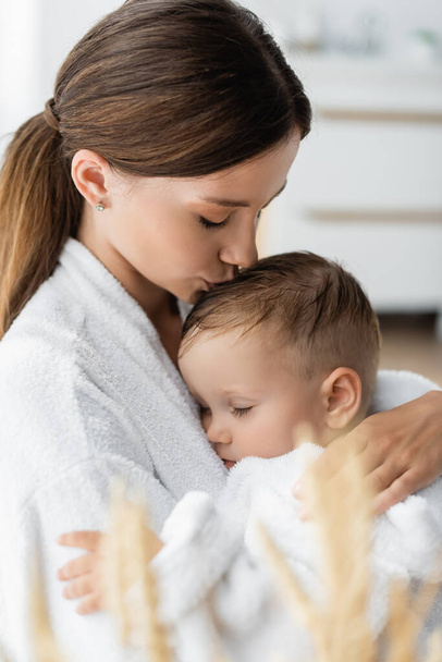 fiatal anya csók fej kisgyermek fia fürdőköpenyben - Fotó, kép