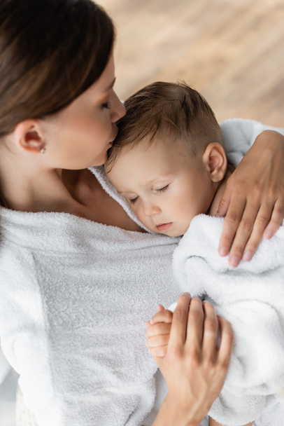思いやりのある母親キス頭の幼児息子で目を閉じてバスローブ - 写真・画像