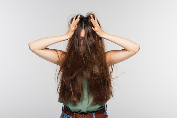 νεαρή γυναίκα προσαρμογή μπερδεμένα μακριά μαλλιά απομονώνονται σε γκρι  - Φωτογραφία, εικόνα