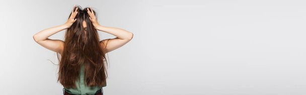 giovane donna che regola i capelli lunghi aggrovigliati isolati su grigio, banner - Foto, immagini