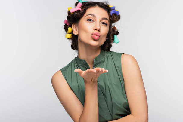 young woman with colorful hair curlers sending air kiss isolated on grey - Foto, Imagen