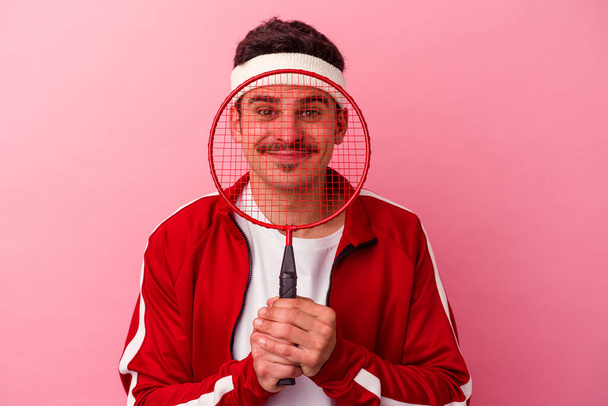 Junger kaukasischer Mann spielt Badminton isoliert auf rosa Hintergrund - Foto, Bild