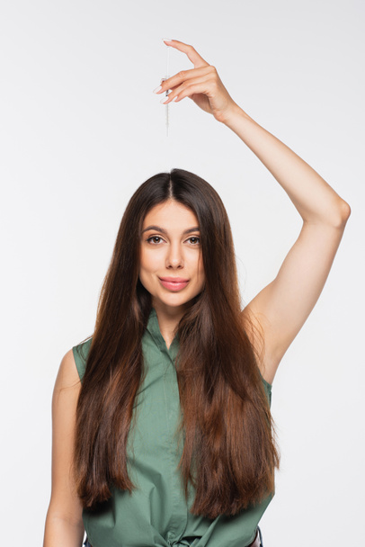 cheerful young woman with shiny hair applying treatment serum on top of head isolated on grey - Photo, Image