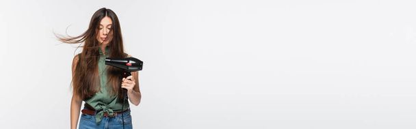 jovem com cabelo brilhante usando secador de cabelo isolado em cinza, banner - Foto, Imagem