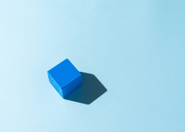 Blue wooden cube with a shadow on light blue background. - Zdjęcie, obraz