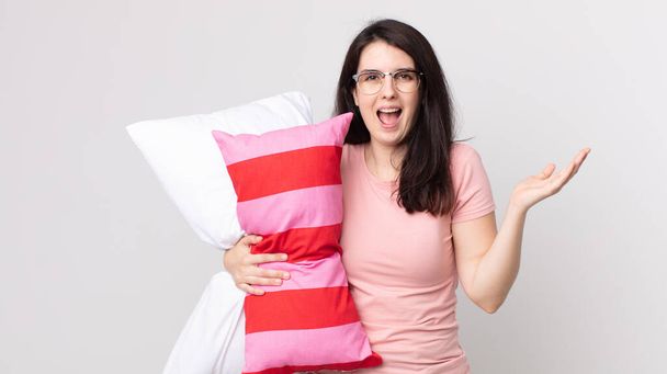pretty woman feeling happy and astonished at something unbelievable wearing pajamas and holding a pillow - Foto, imagen