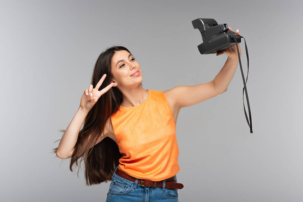 νεαρή γυναίκα κρατώντας vintage φωτογραφική μηχανή και τη λήψη selfie απομονωμένη σε γκρι - Φωτογραφία, εικόνα