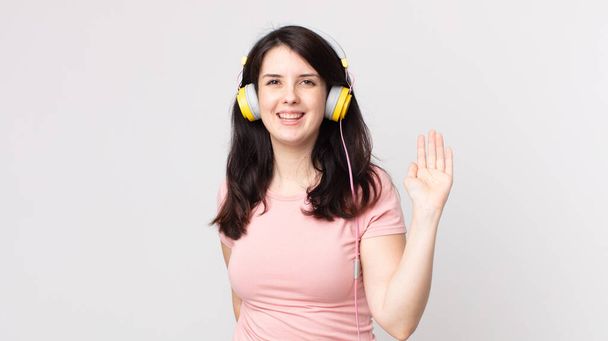 pretty woman smiling happily, waving hand, welcoming and greeting you listening music with headphones - Φωτογραφία, εικόνα