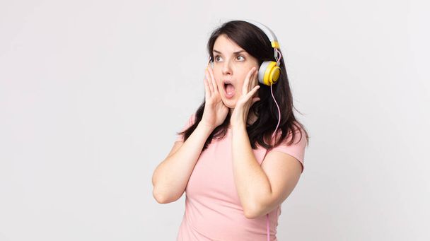 Güzel bir kadın mutlu, heyecanlı ve şaşırmış kulaklıkla müzik dinliyor. - Fotoğraf, Görsel
