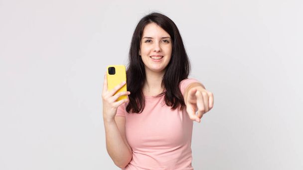 pretty woman pointing at camera choosing you using a smart phone - Fotó, kép
