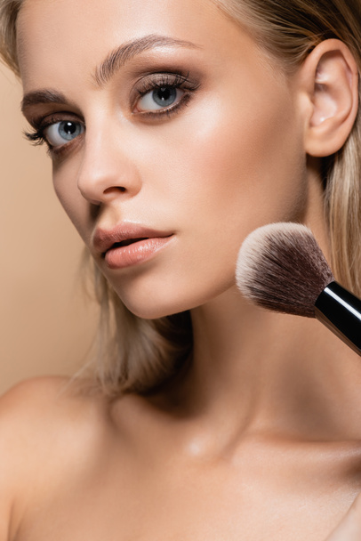 close up view of woman with perfect skin powdering face with soft cosmetic brush isolated on beige - Foto, afbeelding