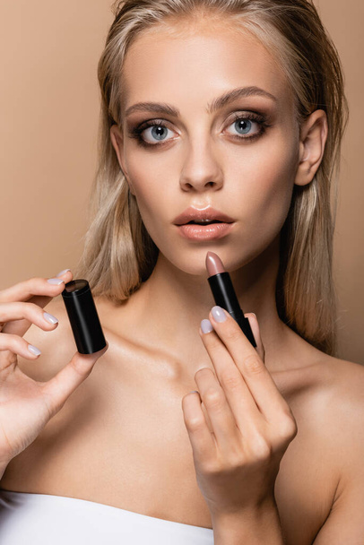 blonde woman with perfect skin and grey eyes holding lipstick isolated on beige - Foto, Imagem