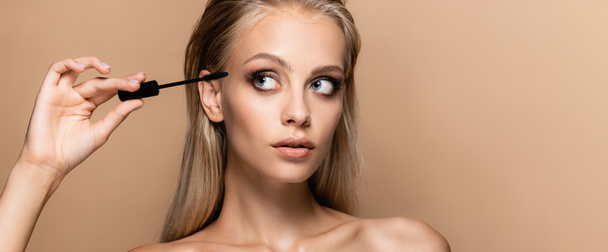 blonde woman with perfect skin and grey eyes holding black mascara isolated on beige, banner - Photo, Image