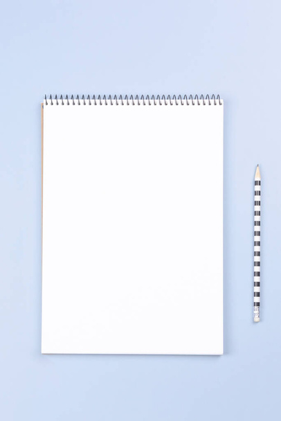Open spiral notebook with blank white page and pencil on light gray desk background. Vertical top view, copy space for text - Foto, Imagen