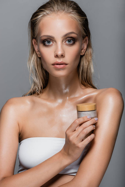 woman with wet skin and hair holding cosmetic cream isolated on grey - Foto, Imagem