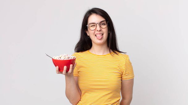 pretty woman with cheerful and rebellious attitude, joking and sticking tongue out and holding a breakfast bowl - Fotó, kép