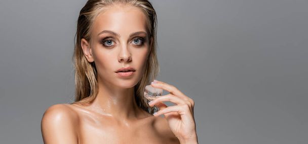 wet woman with perfect skin holding ice cube isolated on grey, banner - Foto, afbeelding