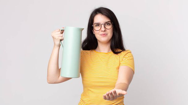 mulher bonita sorrindo feliz com amigável e oferecendo e mostrando um conceito e segurando uma garrafa térmica de café - Foto, Imagem