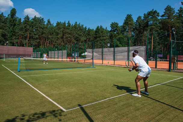 Афроамериканський спортсмен грає в теніс з другом на корті.  - Фото, зображення
