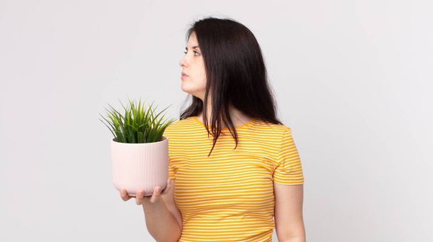 mujer bonita en vista de perfil pensando, imaginando o soñando despierto y sosteniendo una planta decorativa - Foto, imagen
