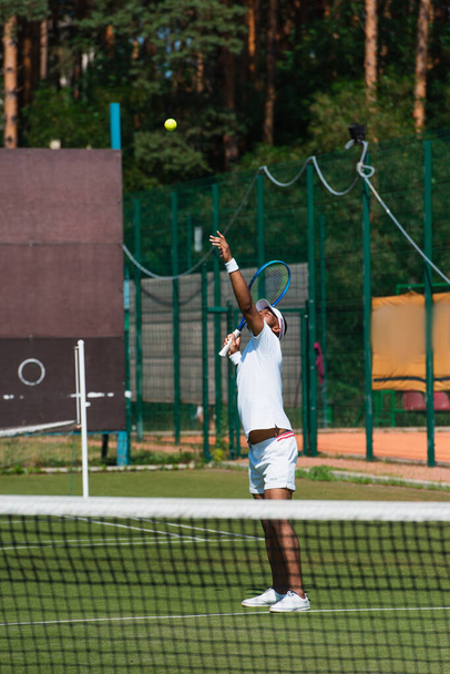 Giocatore di tennis afroamericano che lancia palla vicino alla rete offuscata  - Foto, immagini