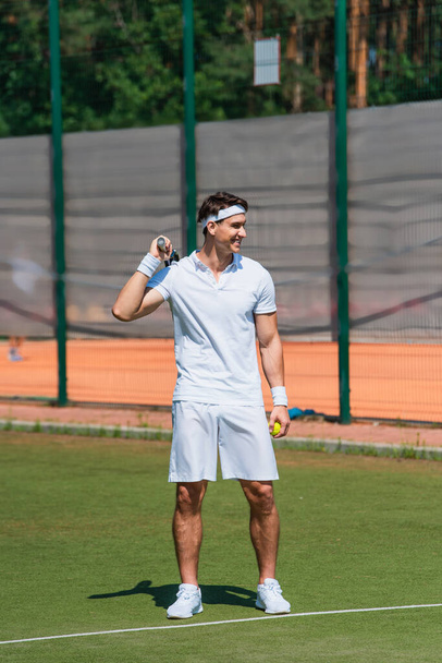 Χαμογελώντας αθλητής κρατώντας ρακέτα τένις και μπάλα στο γήπεδο  - Φωτογραφία, εικόνα