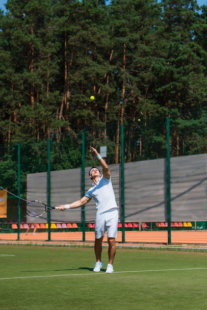 Young sportsman with racket throwing ball while playing tennis on court  - 写真・画像