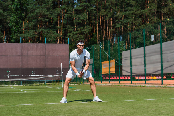 Sportsman in white sportswear holding tennis racket on court  - 写真・画像