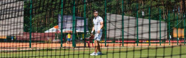 Young man in white sportswear holding tennis racket near blurred net, banner  - Photo, Image