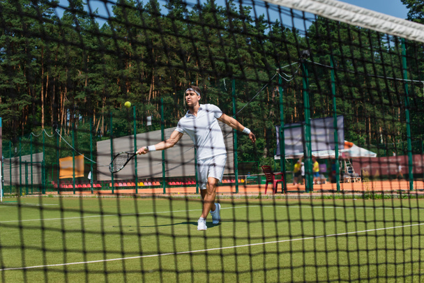 Sportler spielt Tennis auf Platz in der Nähe von verschwommenem Netz  - Foto, Bild