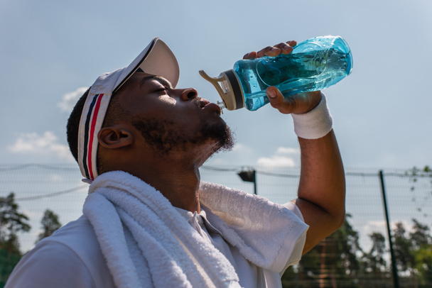 Vista lateral del deportista afroamericano tomando agua al aire libre  - Foto, Imagen