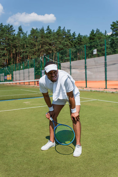 Cansado afroamericano deportista sosteniendo raqueta de tenis en la cancha  - Foto, Imagen