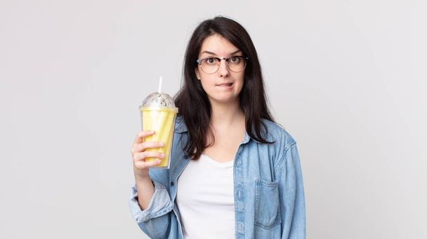 pretty woman looking puzzled and confused and holding a vanilla milkshake - Photo, Image