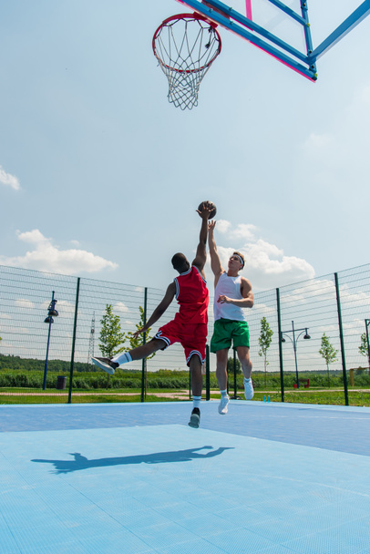 Wide angle view of interracial men jumping while playing streetball outdoors  - Fotografie, Obrázek