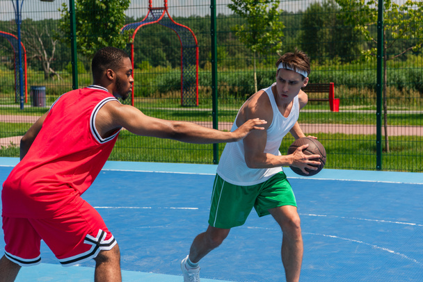 Afroamerikanischer Sportler greift Freund auf Spielplatz mit Basketballball an die Hand  - Foto, Bild