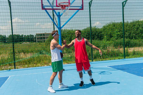 Sorrindo esportistas multiétnicos apertando as mãos no playground streetball  - Foto, Imagem