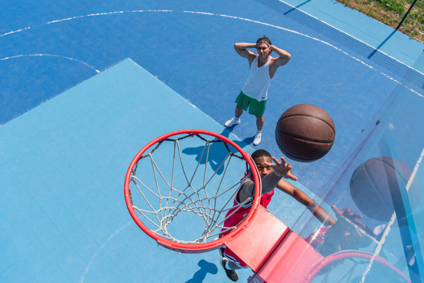 Вид сверху на африканского американского спортсмена, бросающего мяч в обруч на детской площадке для стритбола  - Фото, изображение