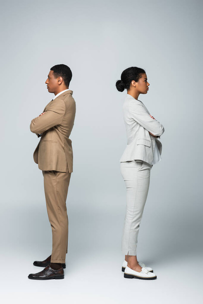 boční pohled na africké americké podnikatele stojící samostatně se zkříženými pažemi na šedé, koncepce rovnosti pohlaví - Fotografie, Obrázek