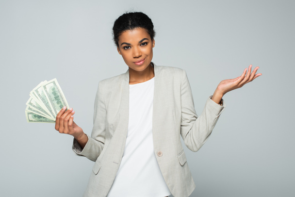 улыбающаяся американская бизнесвумен, держащая долларовые купюры изолированные на сером - Фото, изображение