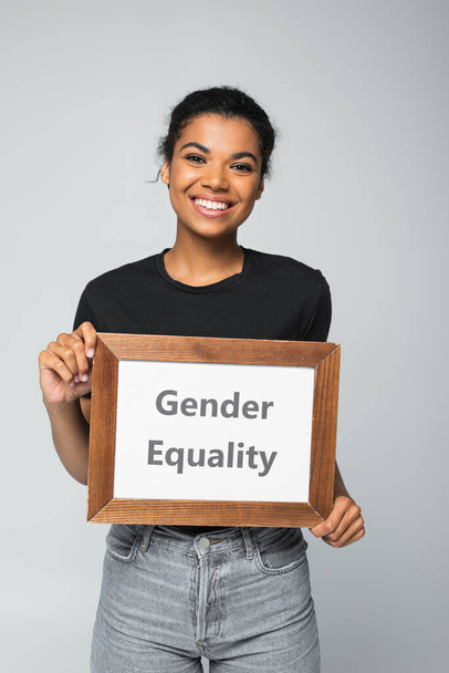 щаслива афроамериканська жінка тримає плакат з написом гендерної рівності ізольовано на сірому
 - Фото, зображення