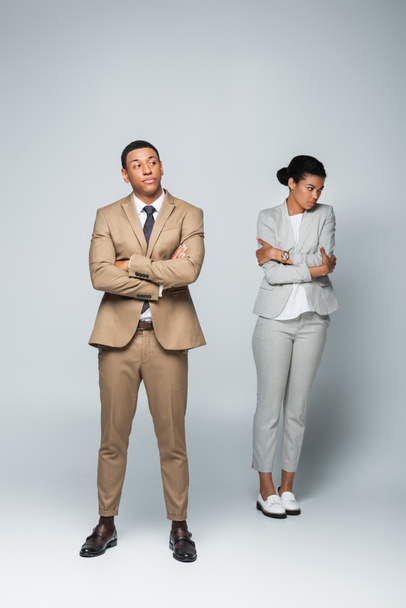 longitud completa de hombre de negocios arrogante con brazos cruzados cerca molesto mujer afroamericana en gris - Foto, imagen